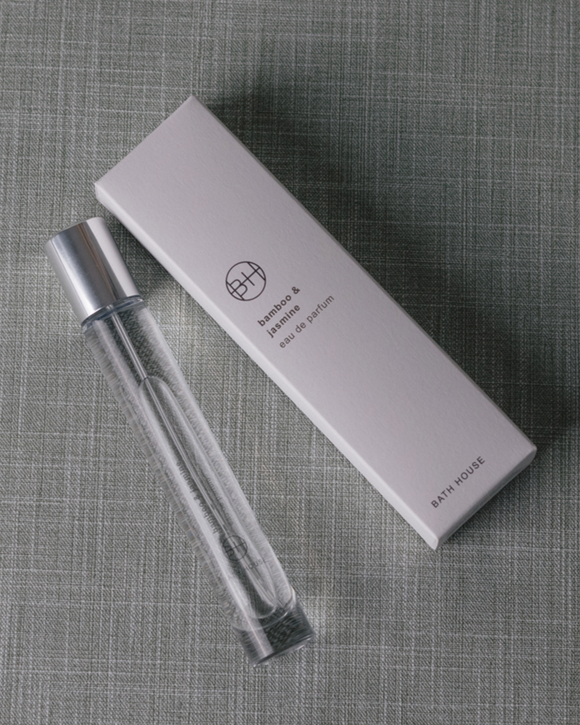 Clear spray perfume bottle with silver top and white box on a textured gray surface