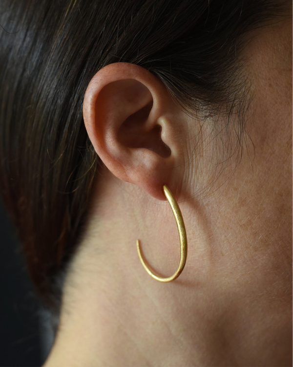 Close-up of a person wearing a gold hoop earring with a dark background