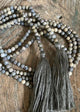 A beaded necklace with gray and brown tones, featuring various designs on the beads, laid out on a wooden surface.